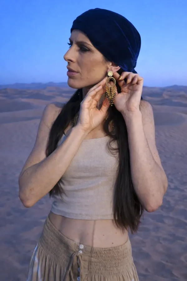 Grandes boucles d’oreilles Amaziga Sacra et féminité gardienne Grandes boucles d’oreilles Amaziga Sacra portées par une femme dans un paysage désertique sous ciel clair