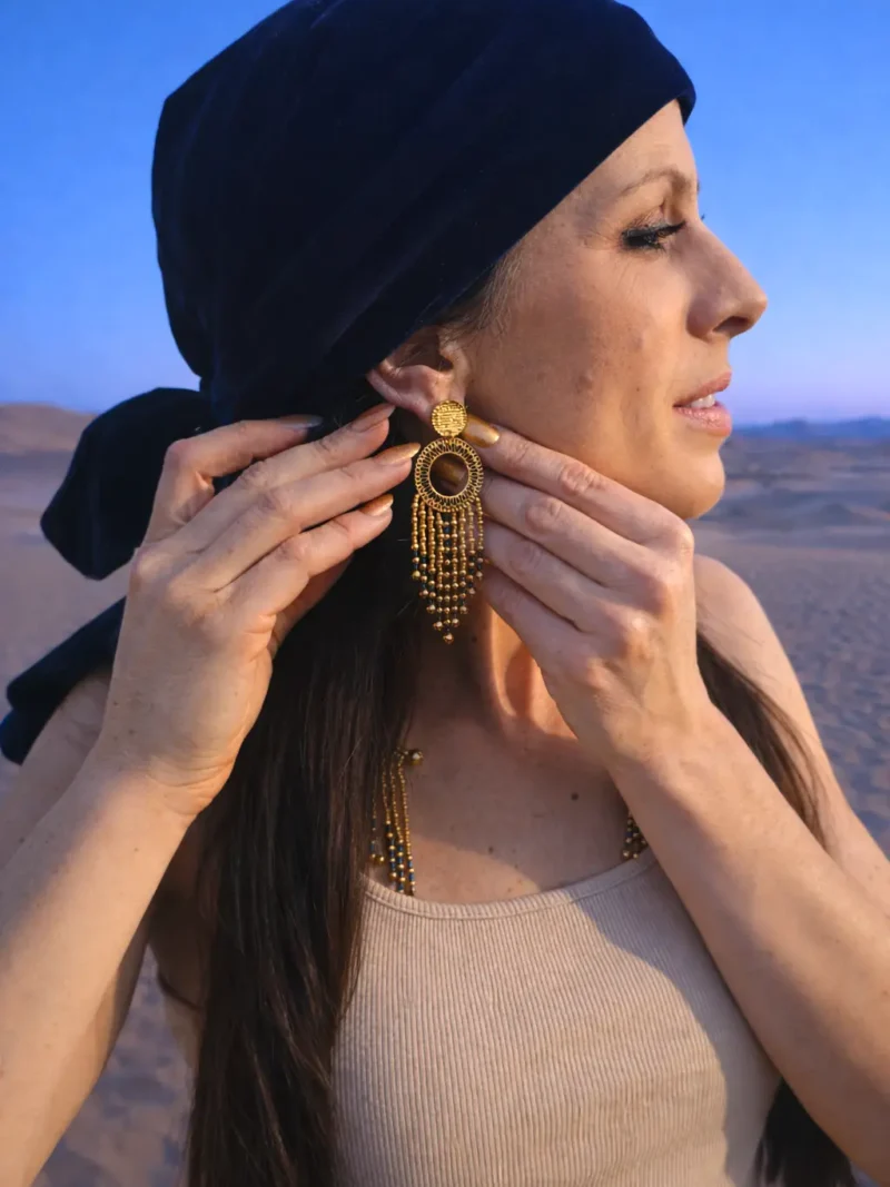 Grandes boucles d’oreilles Amaziga Sacra portées sur la peau avec perles bleues et éléments dorés