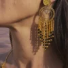 Grandes boucles d’oreilles Amaziga Sacra et détail sacré Les grandes boucles d’oreilles Amaziga Sacra accompagnent l’énergie subtile et la présence intérieure. Inspirées du ciel et des symboles ancestraux, elles soutiennent la fonction de gardienne. Les franges en mouvement évoquent la circulation de l’énergie et la protection invisible. Ce bijou artisanal devient un lien entre visible et invisible, entre corps et cosmos.