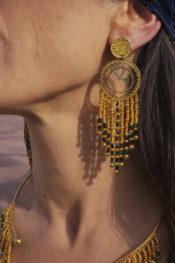 Grandes boucles d’oreilles Amaziga Sacra et détail sacré Les grandes boucles d’oreilles Amaziga Sacra accompagnent l’énergie subtile et la présence intérieure. Inspirées du ciel et des symboles ancestraux, elles soutiennent la fonction de gardienne. Les franges en mouvement évoquent la circulation de l’énergie et la protection invisible. Ce bijou artisanal devient un lien entre visible et invisible, entre corps et cosmos.
