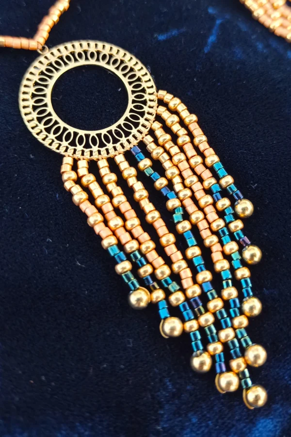 Collier à pendentif Amaziga Sacra posé avec perles bleues et détails dorés sur fond textile Collier à pendentif Amaziga Sacra posé avec perles bleues et détails dorés sur fond textile