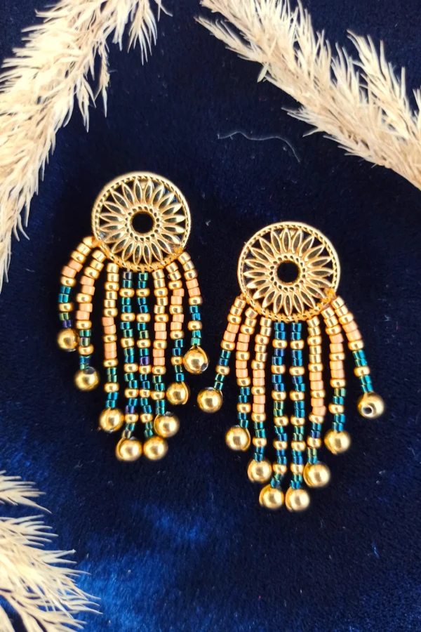 Petites boucles d’oreilles Amaziga Sacra et talisman protecteur Petites boucles d’oreilles Amaziga Sacra posées avec perles bleues et détails dorés sur fond textile