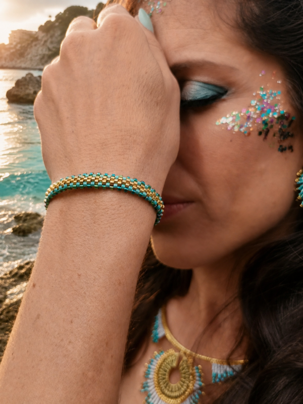 Bracelet Mira Calypsa porté au poignet avec robe bleue et bijoux coordonnés dans un décor naturel lumineux