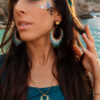 Boucles d’oreilles pendantes Mira Calypsa portées en portrait rapproché avec robe bleue et ambiance poétique Valdyria