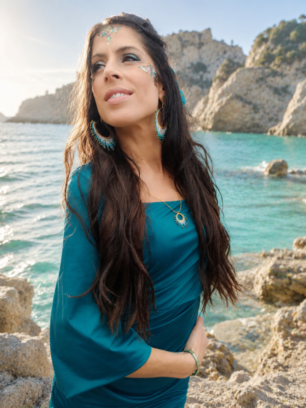 Boucles d’oreilles pendantes Mira Calypsa portées avec robe bleue dans un paysage naturel, bijou artisanal Valdyria