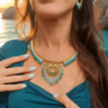 Collier majestueux Mira Calypsa porté en détail avec robe bleue, mains posées et bijou artisanal lumineux