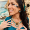 Collier majestueux Mira Calypsa porté avec main sur le décolleté, bijoux coordonnés et décor côtier naturel
