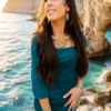 Collier majestueux Mira Calypsa porté avec robe bleue dans une crique lumineuse, bijou artisanal Valdyria en perles Miyuki