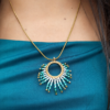 Collier à pendentif Mira Calypsa et création consciente Collier à pendentif Mira Calypsa en gros plan sur robe bleue avec design artisanal turquoise et or