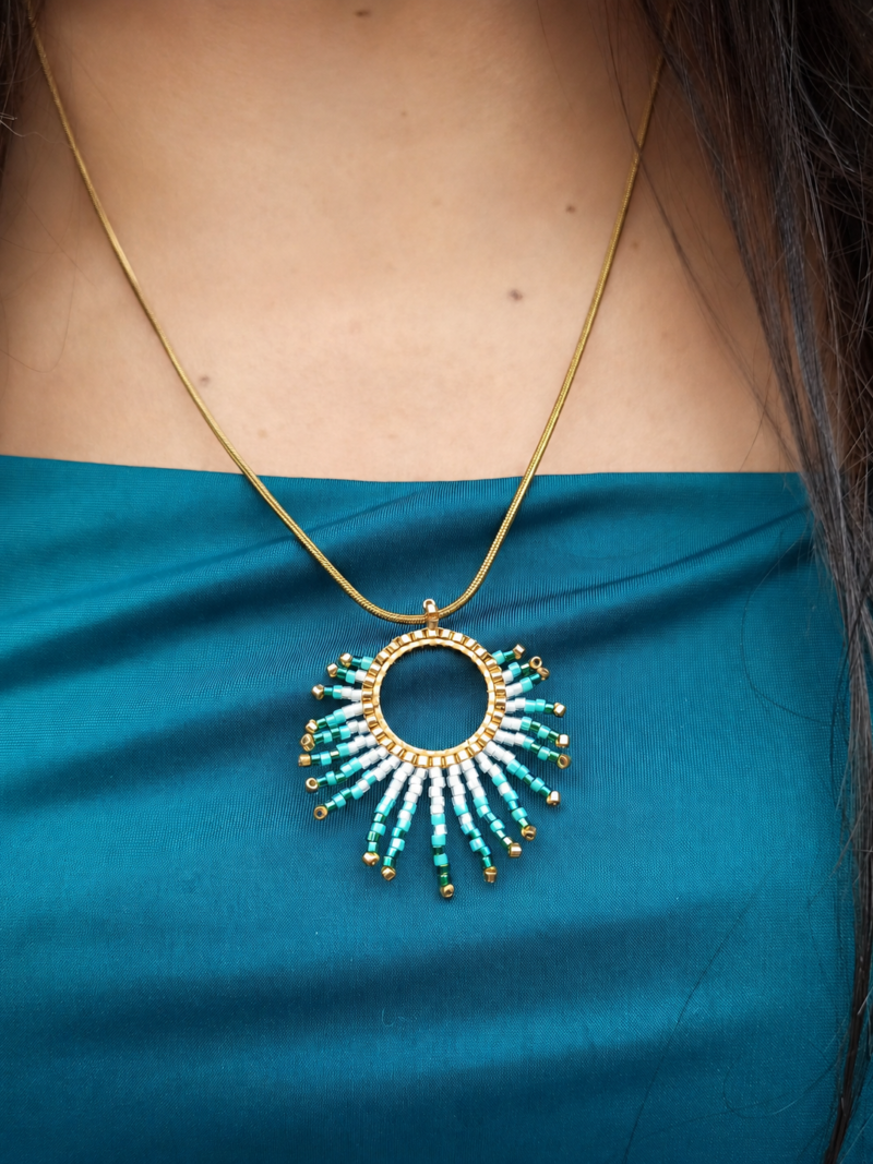 Collier à pendentif Mira Calypsa en gros plan sur robe bleue avec design artisanal turquoise et or