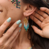 Boucles d’oreilles mini Mira Calypsa en détail portées avec collier assorti dans une ambiance lumineuse et naturelle