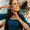 Boucles d’oreilles mini Mira Calypsa portées près du visage dans un paysage côtier doux et lumineux