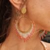 Boucles d’oreilles pendantes Mira Aurora portées en gros plan, bijou artisanal Valdyria en perles Miyuki rose aurore, corail doux et or pâle