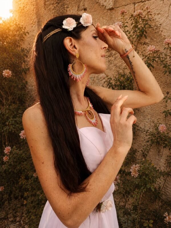 Boucles d’oreilles pendantes Mira Aurora portées avec robe claire dans un décor fleuri, bijou fait main inspiré du recommencement