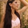 Collier à pendentif Mira Aurora et féminité renaissante Collier à pendentif Mira Aurora porté en portrait avec robe claire et jardin fleuri, bijou artisanal féminin et symbolique