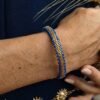 Bracelet Mira Obscura porté assise sur rochers, bijou femme en perles Miyuki bleu indigo et or ancien