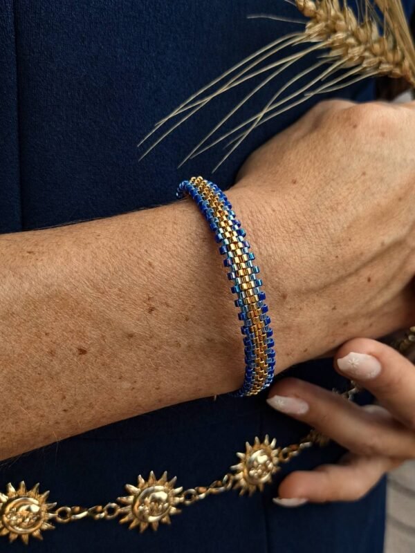 Bracelet Mira Obscura porté assise sur rochers, bijou femme en perles Miyuki bleu indigo et or ancien