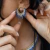 Petites boucles d’oreilles Mira Obscura en gros plan avec perles bleues et dorées, portées près du cou