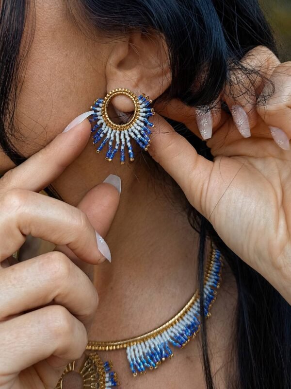 Petites boucles d’oreilles Mira Obscura en gros plan avec perles bleues et dorées, portées près du cou