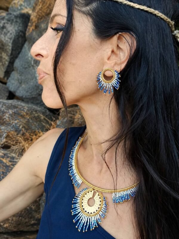 Petites boucles d’oreilles Mira Obscura portées avec collier artisanal sur robe bleu nuit dans un décor rocheux