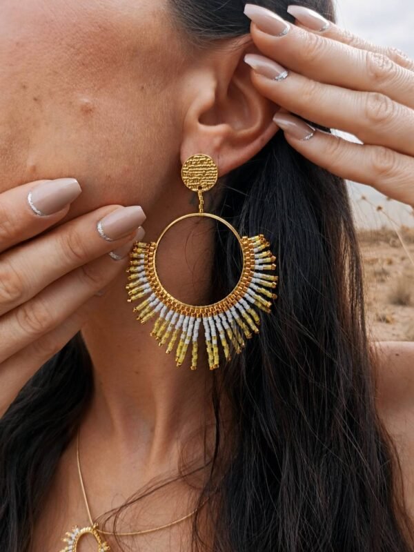 Boucles d’oreilles pendantes Mira Helia et bijou talisman Boucles d’oreilles pendantes Mira Helia portées en gros plan, bijou artisanal Valdyria en perles Miyuki dorées et ambre solaire