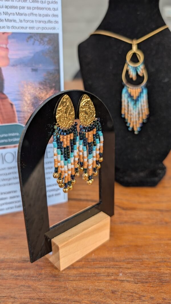 Les petites boucles d’oreilles Nilyra Maria puisent leur identité dans une palette minérale, entre turquoise profond, sable clair et bronze chaud. Ces nuances donnent au bijou une sensation organique, presque terrestre, tout en conservant la précision graphique des perles Miyuki. Fabriquée artisanalement en France, cette pièce Valdyria célèbre la nature, le travail manuel et les créations qui possèdent une véritable présence. Un bijou féminin à la fois sensible, graphique et intemporel.