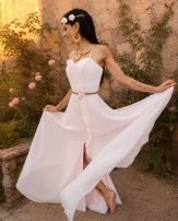 Boucles d’oreilles pendantes Mira Aurora portées avec robe blanche dans un jardin ancien fleuri, bijou artisanal Valdyria inspiré de l’aube