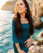 Collier majestueux Mira Calypsa porté avec robe bleue dans une crique lumineuse, bijou artisanal Valdyria en perles Miyuki